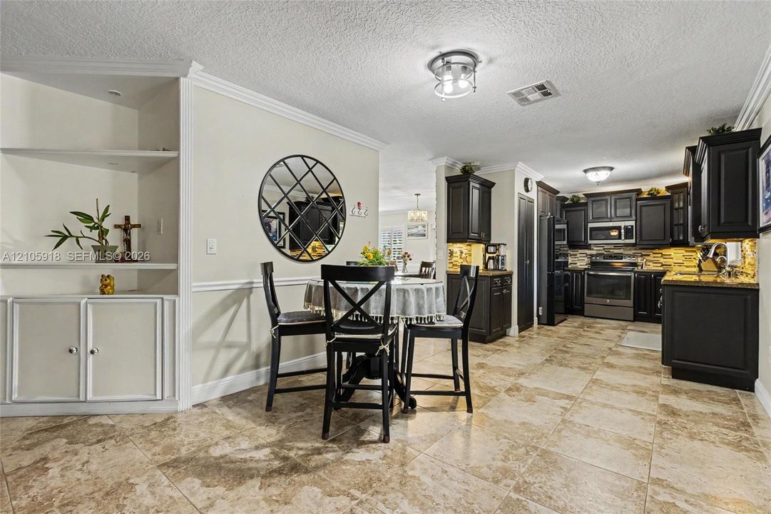 Kitchen featuring dark cabinetry, stone-finish countertops, ceramic tile flooring, and built-in shelving with crown molding