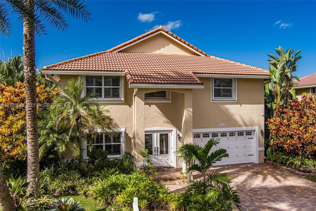 Stucco exterior with a tiled roof, paver driveway, two-car garage, and double-entry front doors