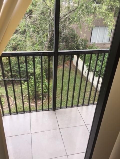 Screened-in balcony featuring ceramic tile flooring and a black metal railing overlooking a landscape of mature trees and foliage