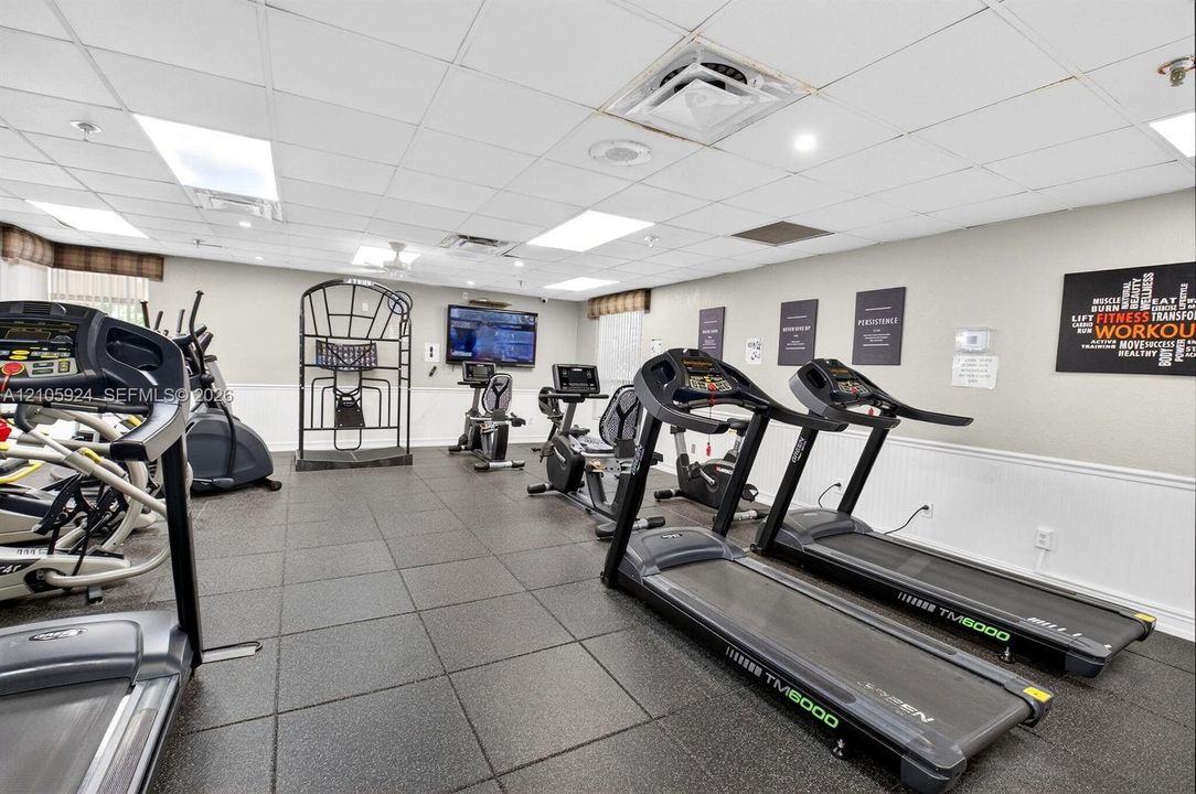Fitness facility featuring rubberized flooring, drop ceiling with recessed lighting, and wall-mounted television