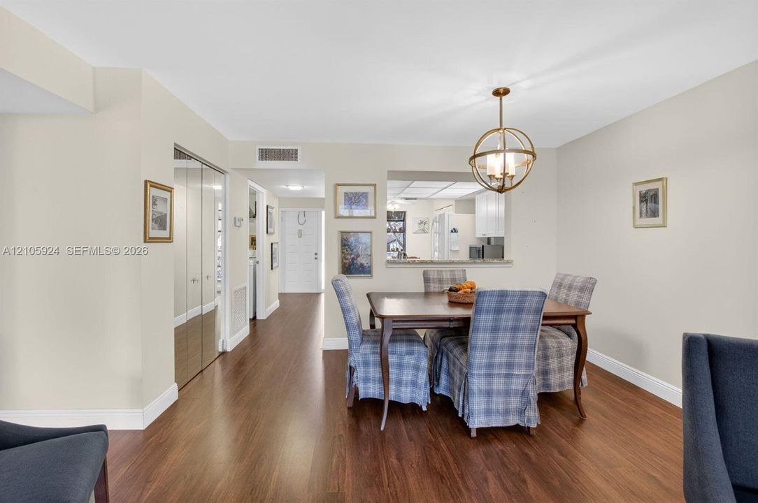 Dining area featuring wood-finish flooring, a spherical metal chandelier, and a pass-through window to the kitchen with a stone-top ledge