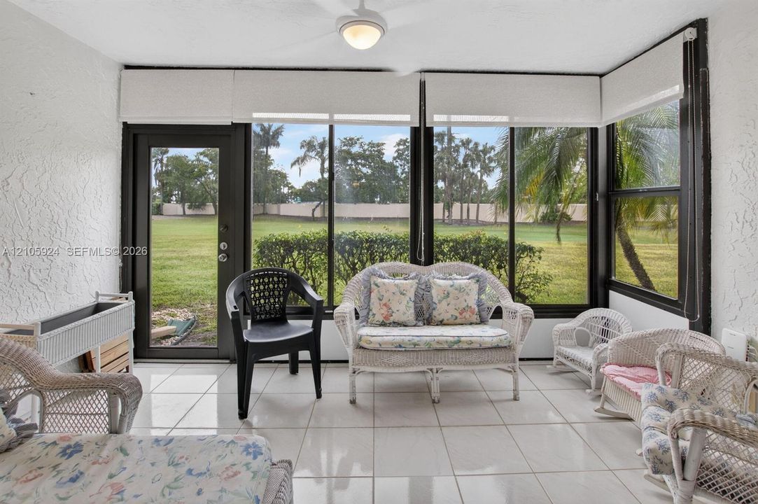 Enclosed sunroom featuring expansive glass walls, a neutral tile floor, a ceiling fan with integrated lighting, and a glass-paneled entry door