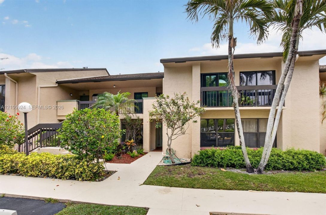 Stucco exterior building featuring second-story balconies with railings, paved walkways, and mature landscaping