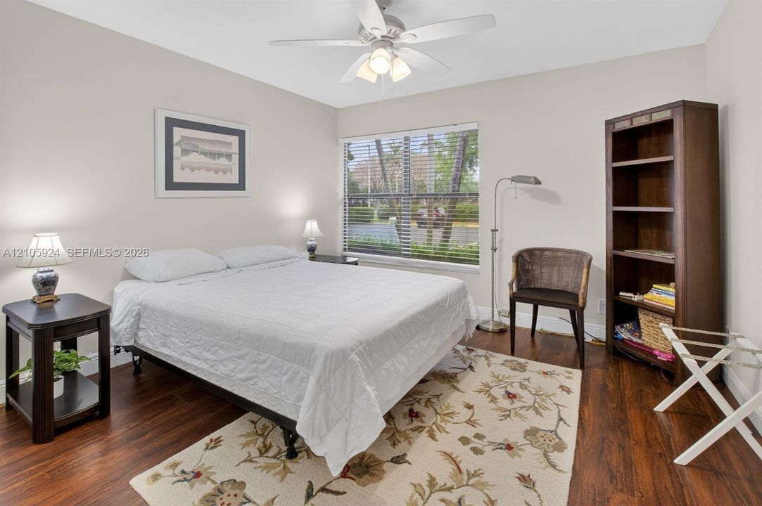 Bedroom featuring wood-finish flooring, a ceiling fan with integrated lighting, and a large window with horizontal blinds