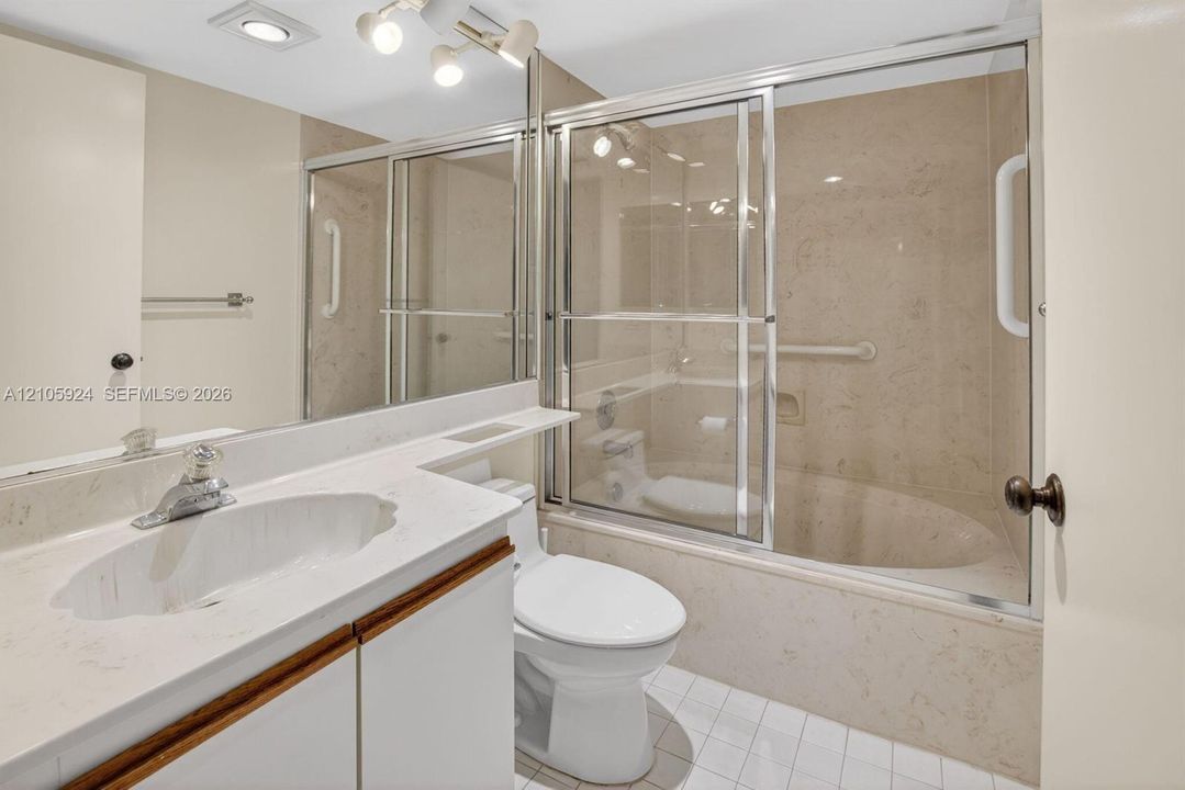 Bathroom featuring a vanity with a white solid-surface countertop, an oval undermount sink, full-width mirror, glass-enclosed shower and tub combination, and tile flooring