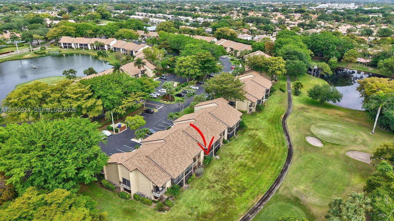 Aerial perspective of multi-unit residential building featuring shingle roofing, exterior balconies, proximity to onsite water features, and immediate access to golf course grounds