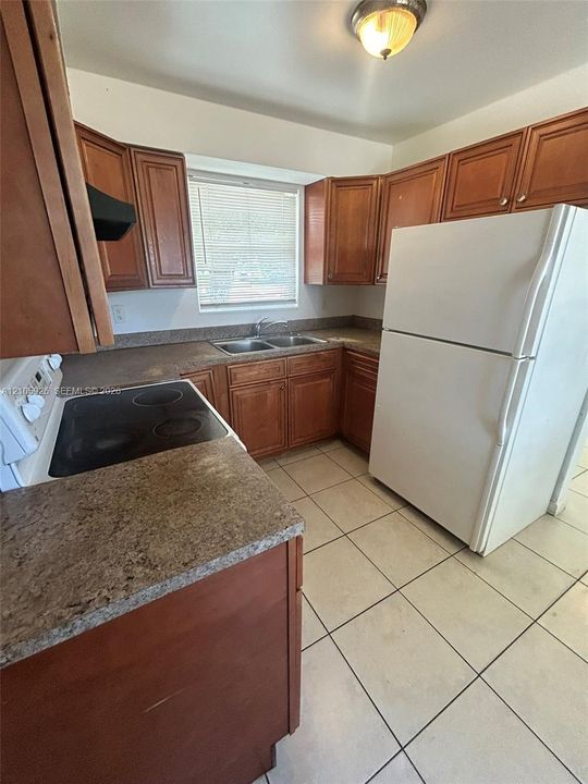 Kitchen featuring wood cabinetry, stone-finish laminate countertops, ceramic tile flooring, a dual-basin stainless steel sink, and a flush-mount ceiling light fixture