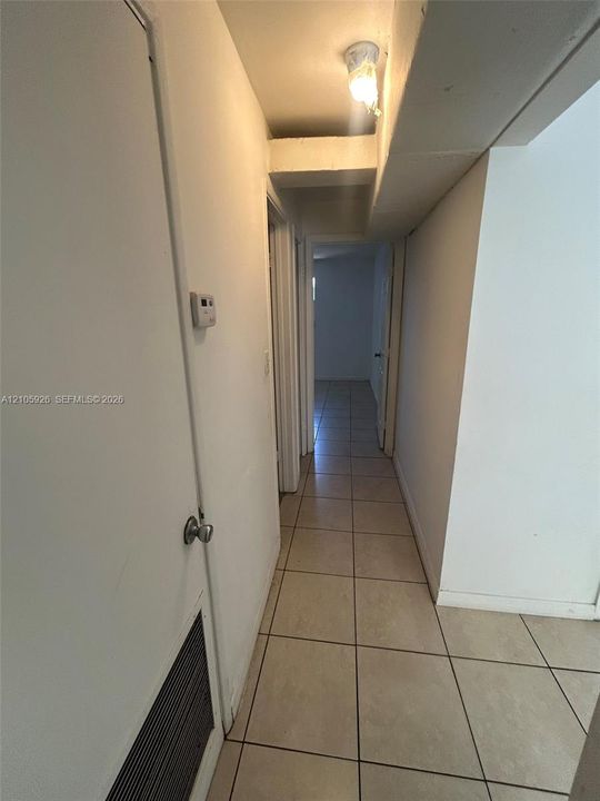 Hallway featuring neutral-toned tile flooring, solid core interior doors, and a ceiling-mounted light fixture