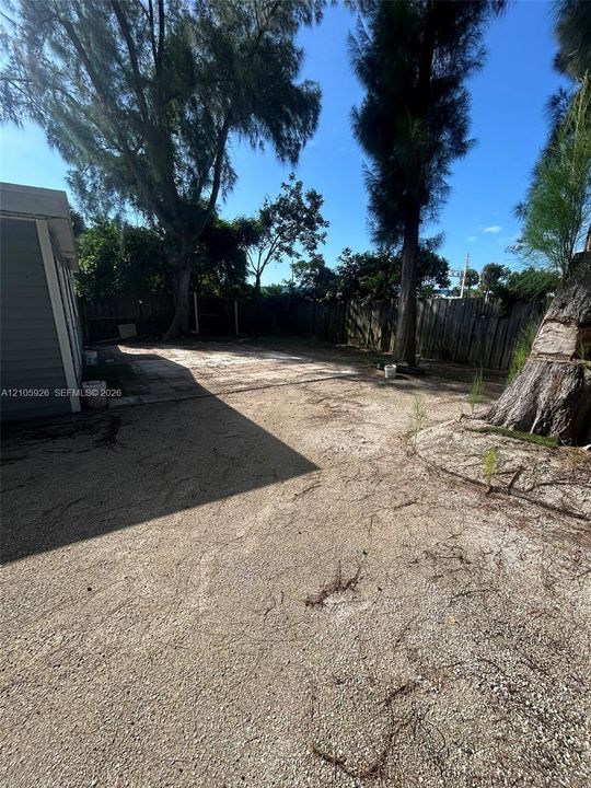 Expansive backyard featuring a concrete patio, perimeter wood fencing, and mature trees