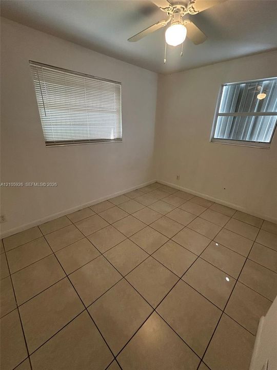 Interior room featuring large-format ceramic tile flooring, neutral wall finishes, multi-pane windows with horizontal blinds, and a central ceiling fan with an integrated light fixture