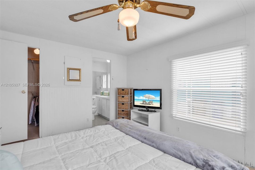 Bedroom featuring white wainscoting, horizontal slat blinds, and an overhead ceiling fan with light fixture