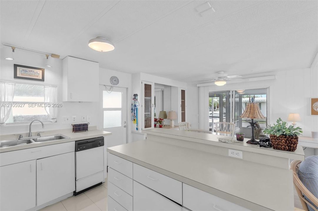 Kitchen featuring white cabinetry, solid-surface countertops, dual-basin stainless steel sink, built-in dishwasher, and a raised breakfast bar