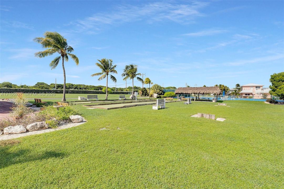Expansive lawn featuring bocce courts, a thatched-roof pavilion, mature palm trees, and stone hardscaping