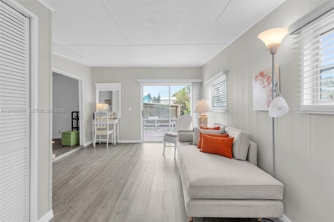 Living area featuring vertical panel wall detailing, wood-finish flooring, louvered closet doors, and a sliding glass door providing external access
