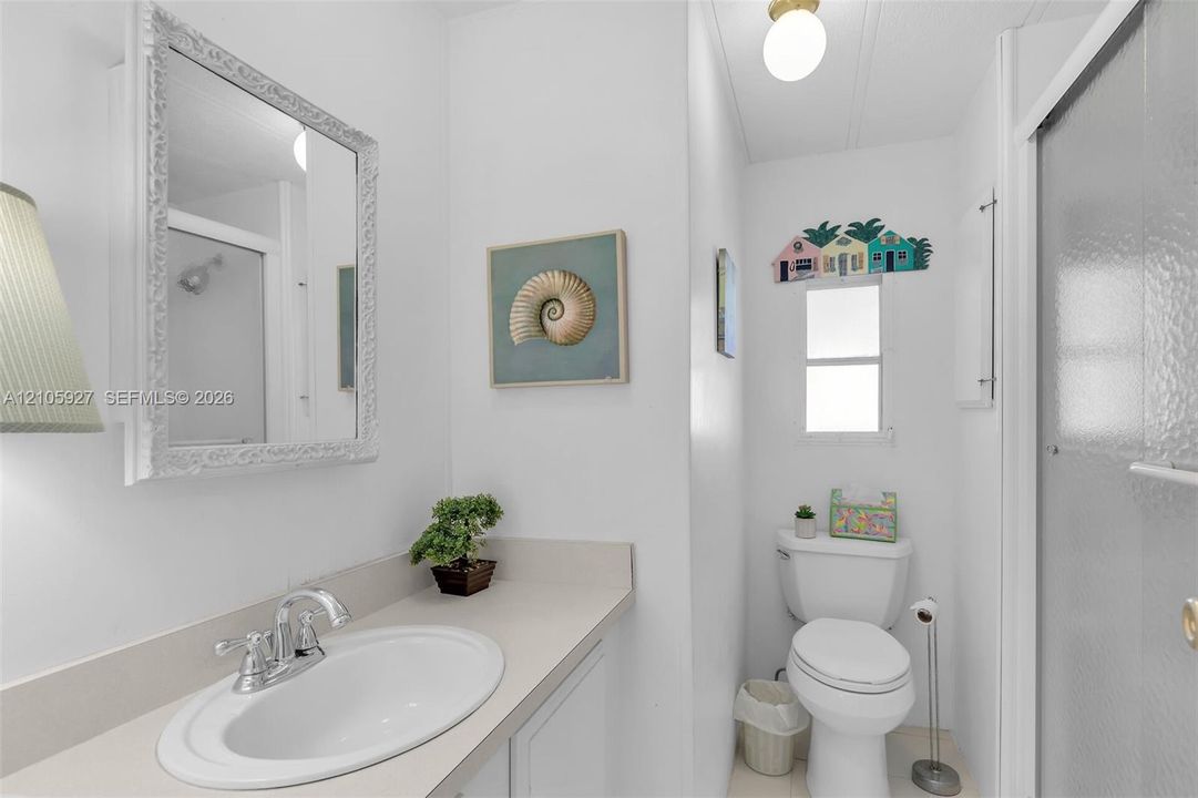 Bathroom featuring a vanity with a solid-surface countertop, an integrated oval basin, a chrome double-handle faucet, a framed wall mirror, and a glass-enclosed shower