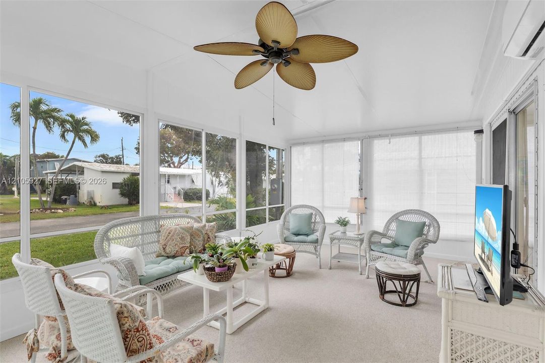 Enclosed sunroom featuring floor-to-ceiling windows, wall-mounted climate control unit, and overhead palm-style ceiling fan