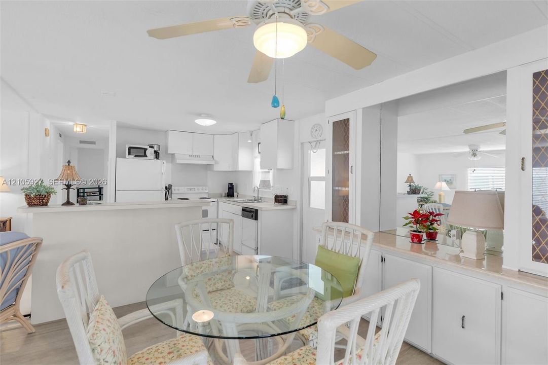 Kitchen featuring white cabinetry, integrated appliances, and a pass-through counter, accompanied by a dining area with built-in cabinetry and a ceiling fan
