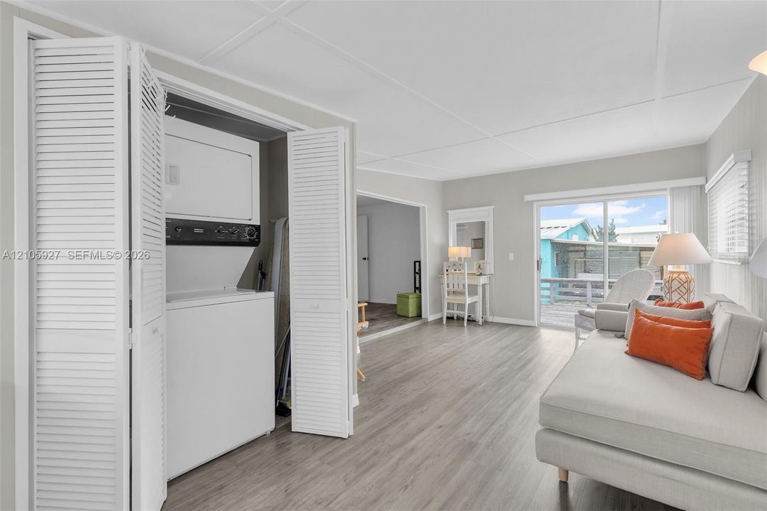 Utility closet featuring stacked laundry appliances and bi-fold louvered doors, wood-finish flooring, and a sliding glass door