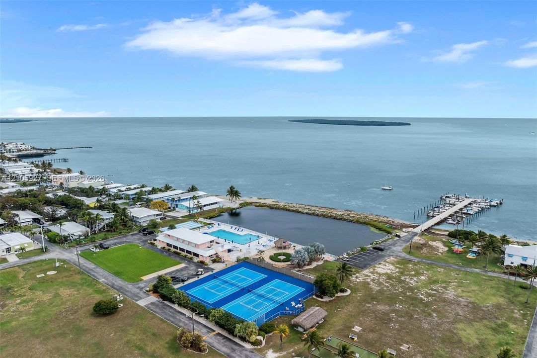 Coastal community featuring two tennis courts, an outdoor swimming pool, a grass lawn, and a private dock