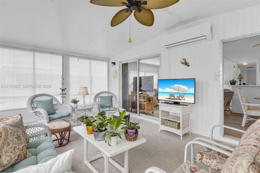 Sunroom featuring floor-to-ceiling windows, vaulted ceiling with integrated fan, and wall-mounted ductless climate control unit