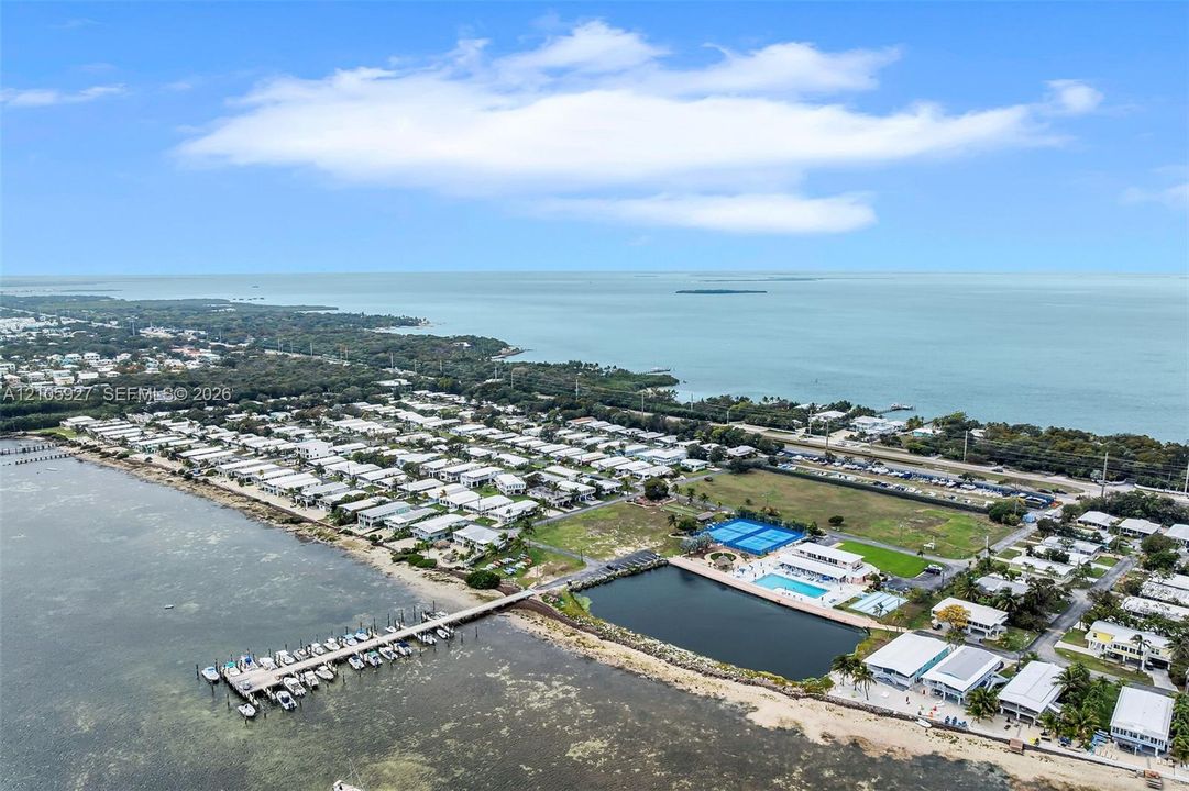 Aerial perspective featuring a waterfront location, a private dock with multiple slips, a swimming pool, and two hard-surface tennis courts