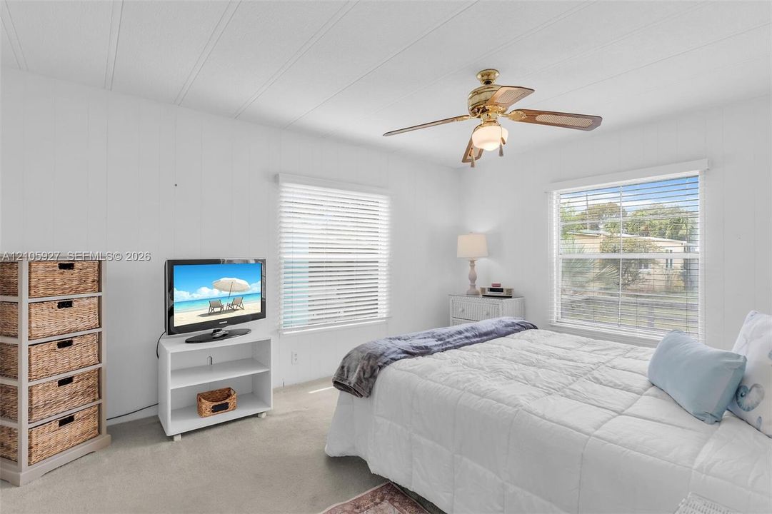 Bedroom featuring neutral carpeting, panel walls, dual windows with horizontal blinds, and a ceiling fan with integrated lighting