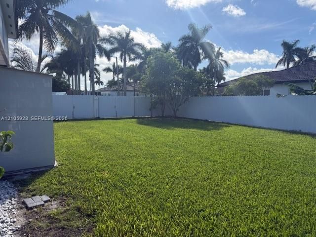 Expansive backyard featuring a manicured lawn, white vinyl perimeter fencing, and mature palm trees