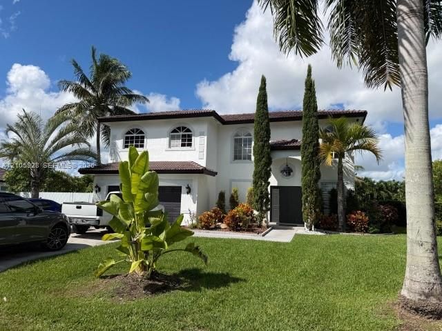 Two-story residence featuring white stucco exterior, arched window detailing, dark tile roofing, and manicured landscaping