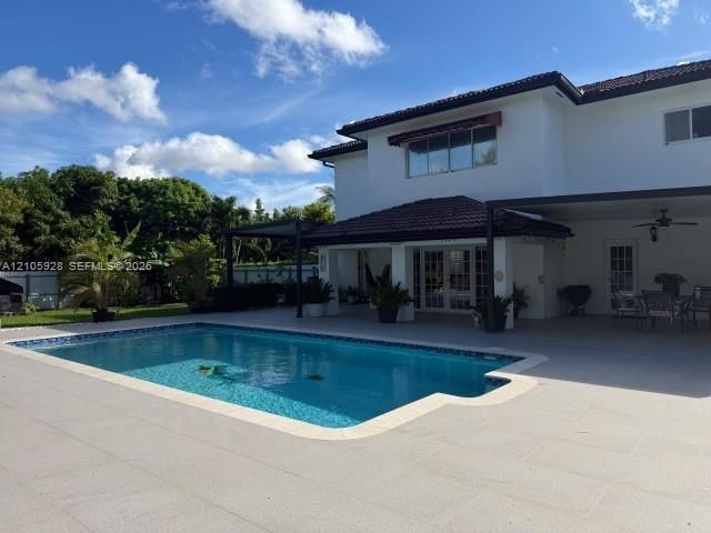 In-ground pool featuring a tile border, expansive stone-paver deck, and a covered lanai