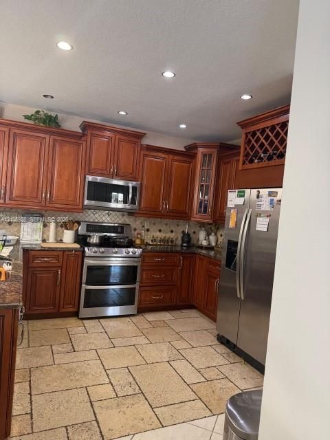 Kitchen featuring dark wood cabinetry, integrated wine storage, natural stone flooring, stainless steel appliances, and recessed lighting