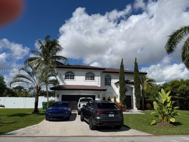 Two-story residence with a tile roof, stucco exterior, arched window detailing, and a concrete driveway leading to a multi-car garage