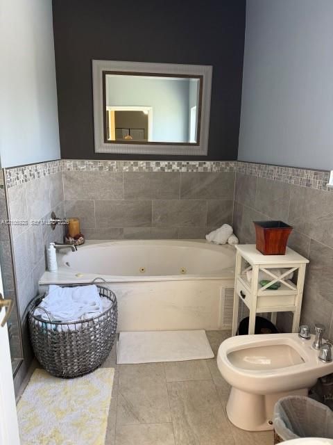 Jetted soaking tub with tile surround, mosaic accent trim, wall-mounted faucet, and porcelain floor tile featuring a bidet