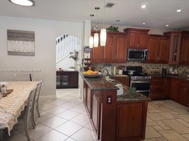 Kitchen featuring raised-panel wood cabinetry, stone countertops, stainless steel appliances, pendant lighting, and ceramic tile flooring