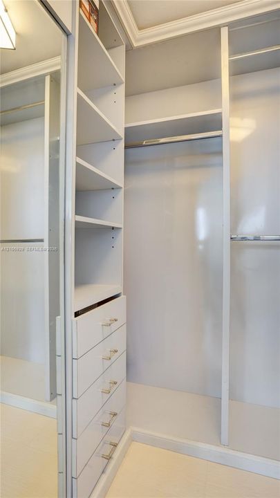 Custom walk-in closet featuring white built-in shelving, a five-drawer dresser unit with metallic pulls, dual hanging rods, and a full-length mirrored door