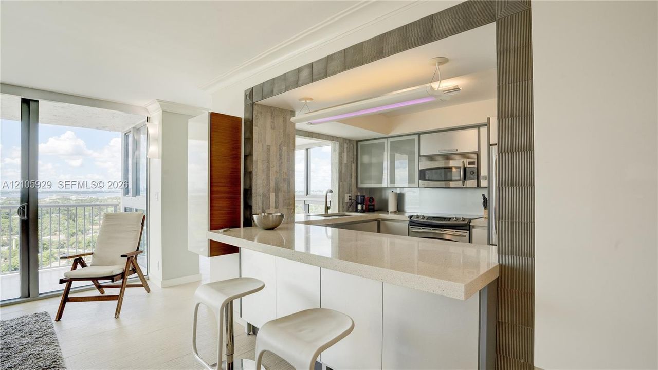 Kitchen featuring a stone-surface breakfast bar, glass-front cabinetry, stainless steel microwave, and metallic tile trim framing