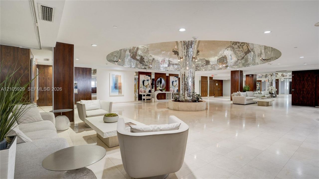 Expansive lobby featuring polished stone flooring, dark wood-finished paneling, recessed lighting, and a prominent central circular ceiling feature with a reflective metallic finish
