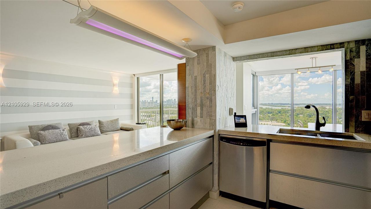 Kitchen featuring flat-panel cabinetry, light-toned stone-finish countertops, stainless steel appliances, a high-arc matte black faucet, and integrated linear lighting