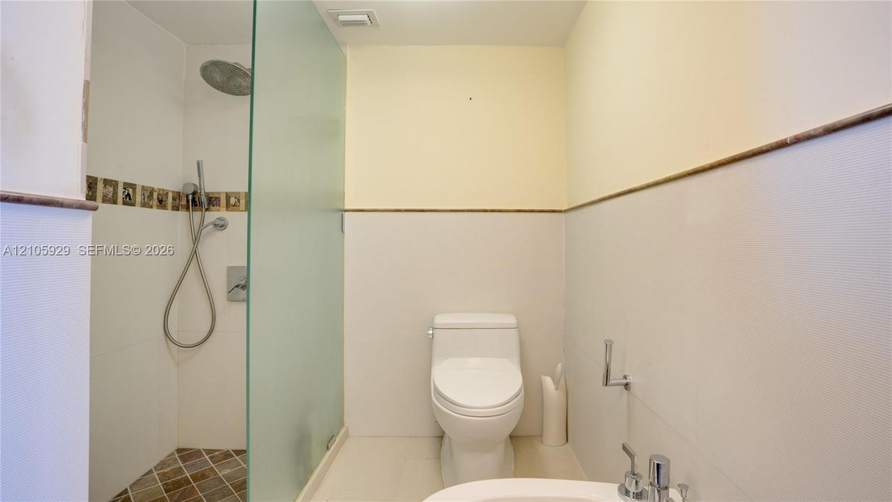Walk-in shower featuring a frosted glass partition, rainfall showerhead, and tiled flooring, accompanied by a low-profile toilet and bidet
