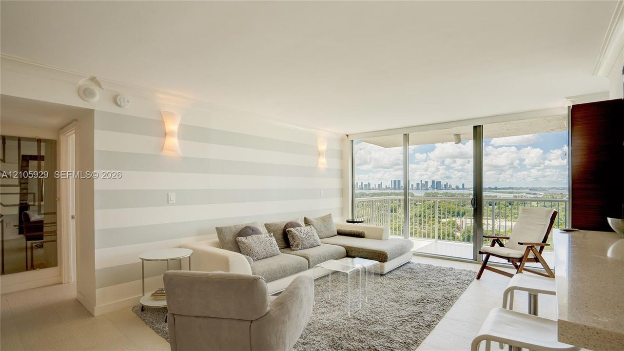 Floor-to-ceiling sliding glass doors, private balcony, neutral-toned striped accent wall, integrated wall sconce lighting, and light-toned tile flooring