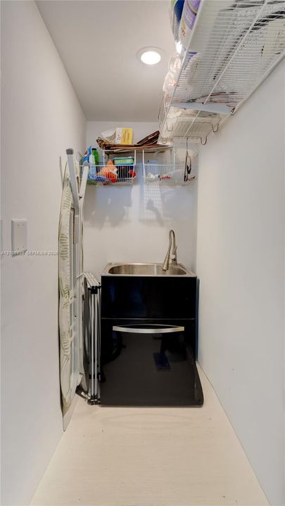 Utility area featuring a stainless steel drop-in sink, high-arc pull-down faucet, black cabinetry, and built-in wire shelving