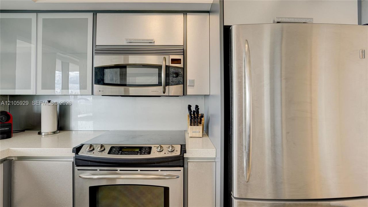 Kitchen featuring high-gloss cabinetry, stone-finish countertops, stainless steel appliances, and a smooth-top electric range