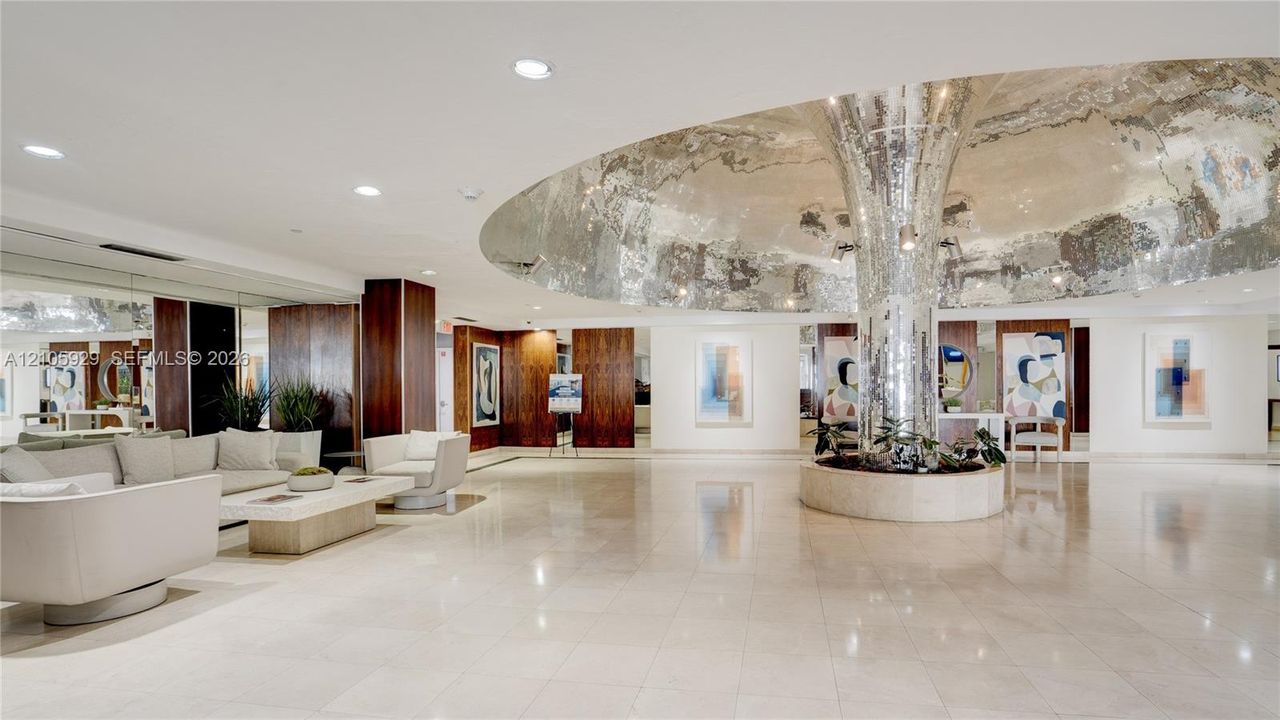 Grand lobby featuring polished stone flooring, a mirrored central structural column, recessed ceiling lighting, and wood-paneled wall accents