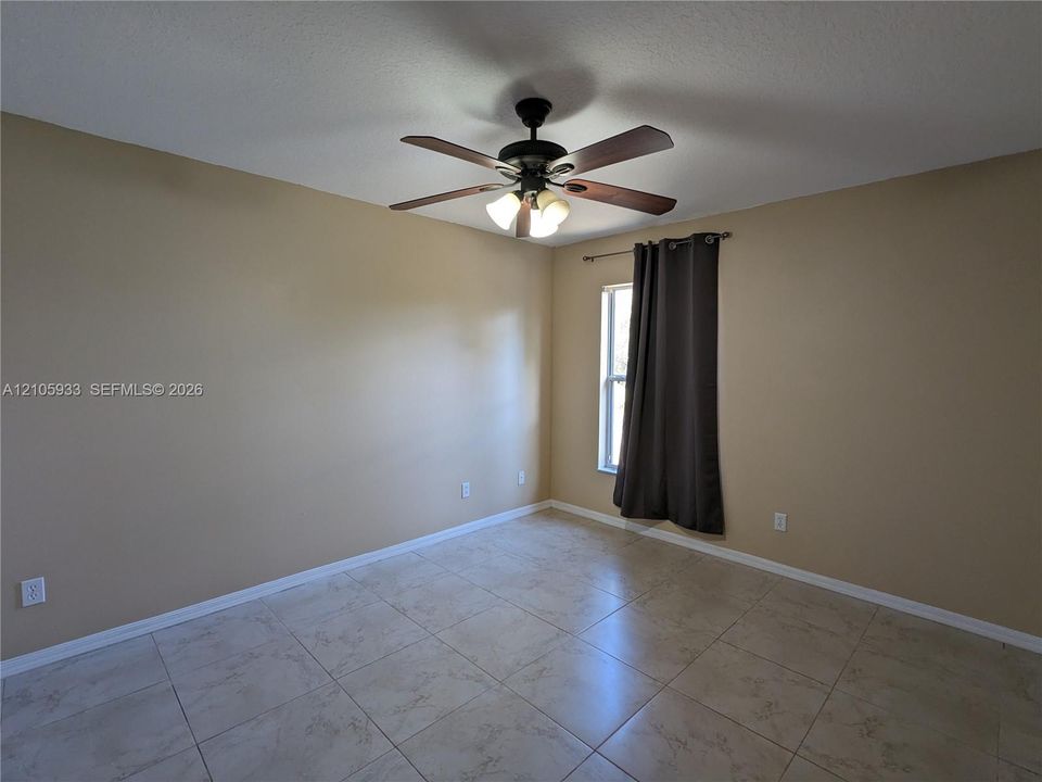 Room featuring large-format ceramic tile flooring, neutral wall paint, and a ceiling-mounted fan with integrated multi-bulb light fixture