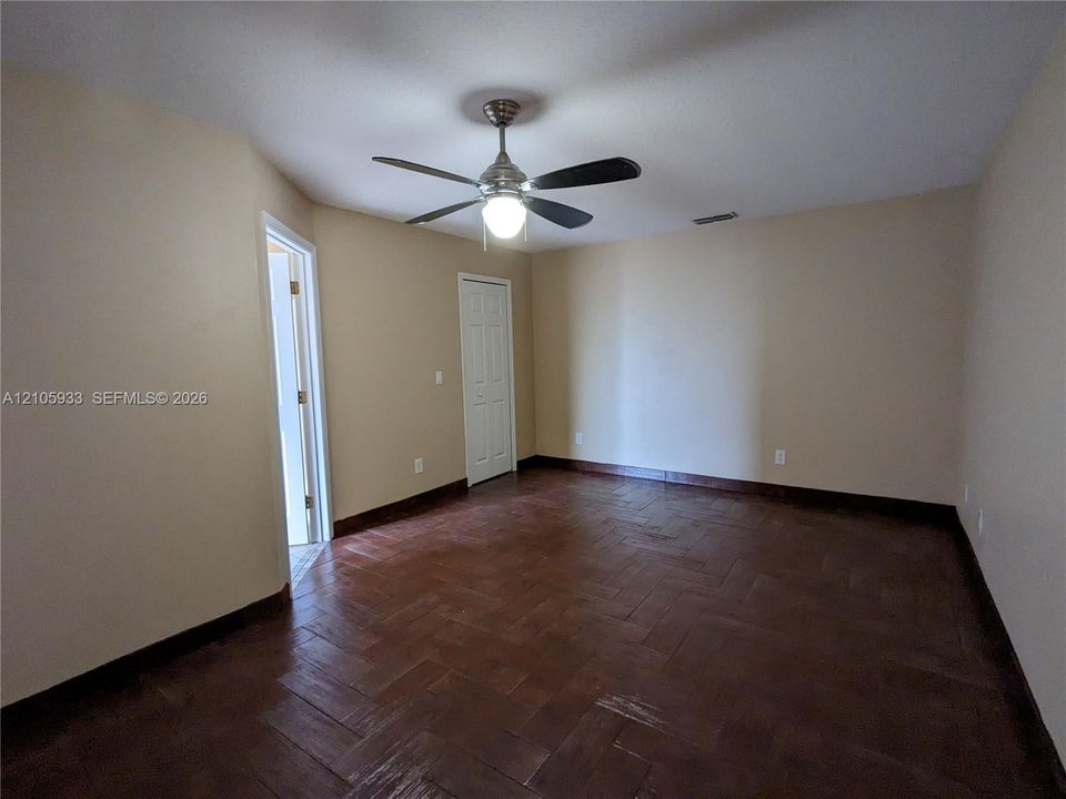 Herringbone-patterned wood-finish flooring, brushed nickel ceiling fan with integrated light fixture, and six-panel interior doors