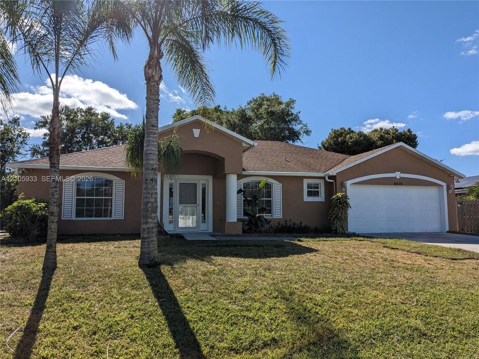 Stucco exterior featuring an arched entryway, column detailing, multi-pane windows with decorative shutters, and an attached two-car garage