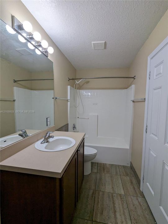 Bathroom featuring a dark wood-finish vanity with a solid-surface countertop, an integrated oval sink, a wall-to-wall vanity mirror with an attached five-bulb light fixture, and tile flooring