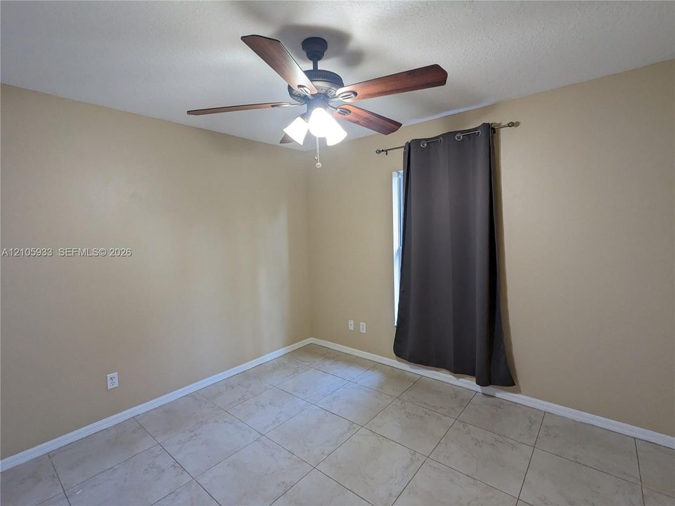 Neutral-toned interior space featuring light-colored tile flooring and a ceiling-mounted fan with integrated lighting