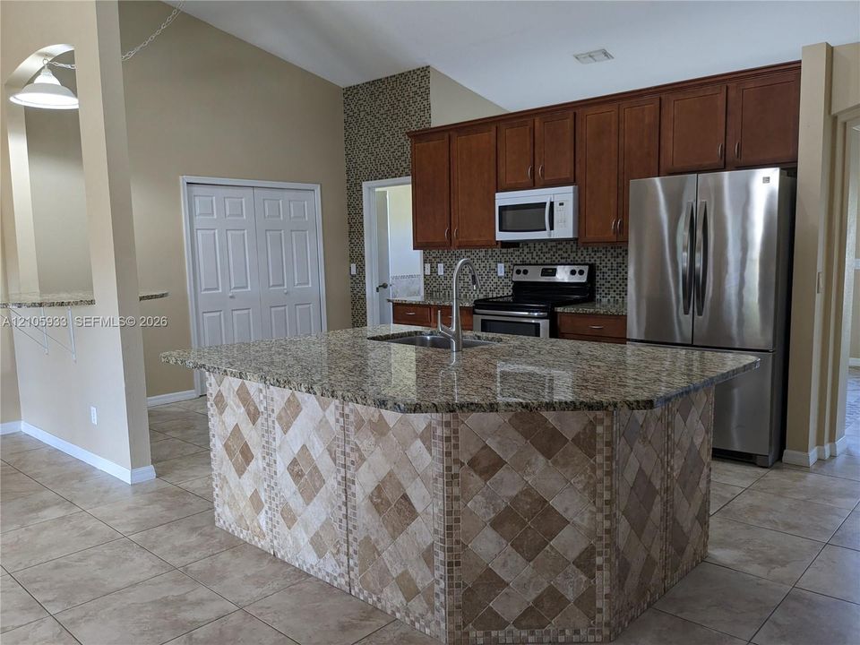 Kitchen featuring a center island with stone-finish countertops, tiled island base, vaulted ceiling, wood cabinetry, and stainless steel appliances
