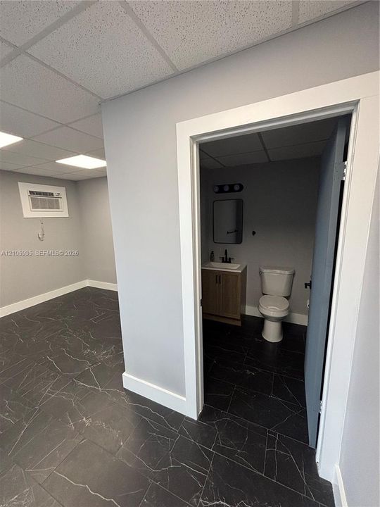 Room featuring large-format dark stone-finish tile flooring, drop ceiling with recessed lighting, and a wall-mounted cooling unit