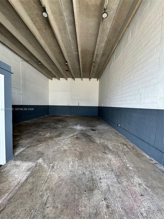Industrial interior featuring exposed concrete beam ceiling, painted brick walls, finished concrete flooring, and track lighting